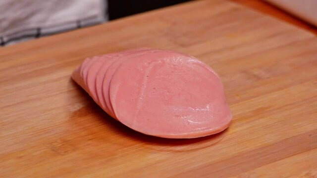 Close-up of female hands pouring ham bologna out of vacuum sealer bags on the cutting board. Concept of preparing healthy meal.
