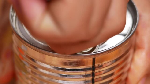 Hands opening canned food, close-up. Showing how to open a can with pull tab. Non-perishable food storage products in the home kitchen.