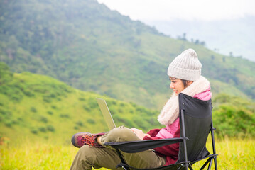 Asian woman sitting on outdoor chair with drinking hot coffee and looking to beautiful nature of mountain. Beautiful female relax and enjoy outdoor lifestyle hiking and camping in summer vacation.