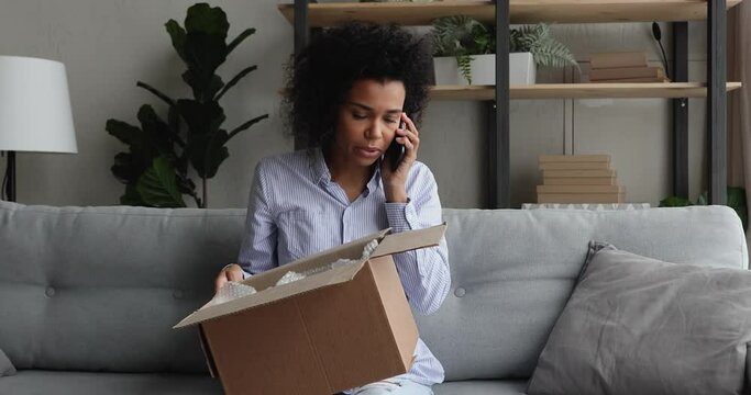 Unhappy millennial african ethnic female client feeling dissatisfied with received item, telling complaints in mobile phone call. Stressed young mixed race client having negative shopping experience.