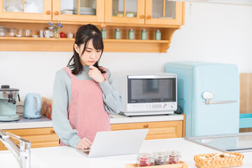 Fototapeta na wymiar キッチンでパソコンを見る女性　考える