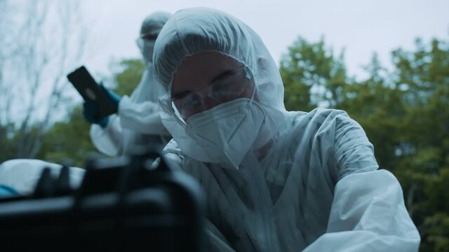 Criminalists discovering knife at crime scene close-up, taking evidence from accident, murder. Investigating proof for forensic examination. Detective workers, medical examiners.