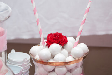 big white gumballs in a crystal container with a red flower on top and two pink and white paper straws