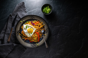 Top down view of a Korean noodle dish topped with a fried egg, against a dark background.