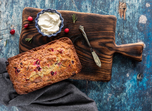 Top down view of a cranberry rosemary loaf on a wooden board, ready to be sliced.