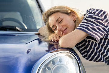Middle woman driver dreaming, embracing hood of car after detailing, polishing. Happy female...