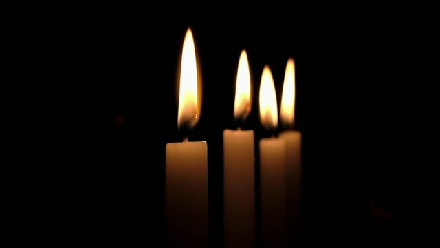 Flames of four candles flicker in darkened room