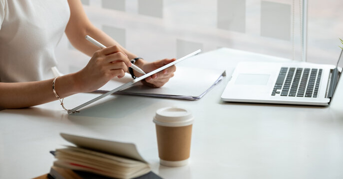 Young business woman hands holding pen stylus and working on black digital tablet pc with laptop computer on the desk at modern home office. Remote working, online learning concept