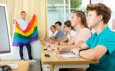 School teacher with flag explains to students what is LGBT in schoolroom