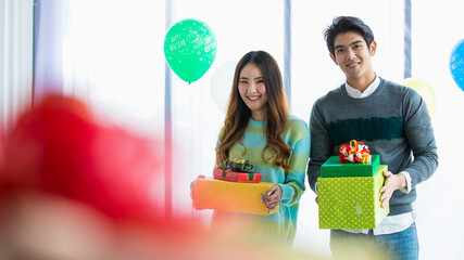 Sweet young Asian couples closely standing together, carrying gift box, lovely smile and happy for...