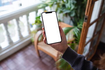 Mockup image of a woman holding mobile phone with blank desktop screen on balcony at home