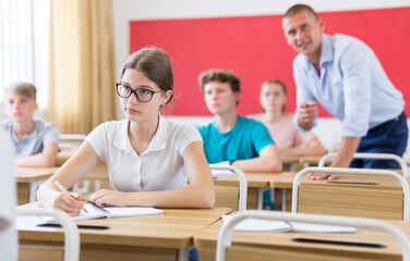 Fototapeta premium Teen girl listening to lecturer and writing in notebook in classroom