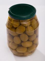 Marinated whole green olives in glass jar on white surface. Organic snack