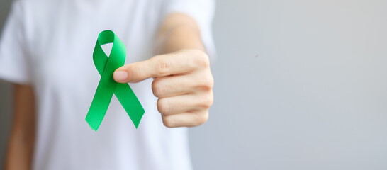 Hand holding green Ribbon for Liver, Gallbladders, bile duct, cervical, kidney Cancer and Lymphoma Awareness month. Healthcare and world cancer day concept