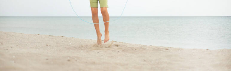 A boy on a sandy beach is jumping rope. Legs close up. Sports activities by the sea. Healthy lifestyle.