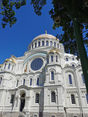 Obraz premium St. Nicholas Cathedral among the trees against the background of a cloudless sky, on a summer day in Kronstadt.