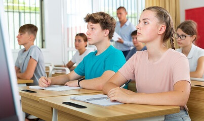 Pupils sitting in class and listening carefully to male teacher.