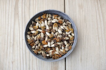 Dried marigold flowers in a round tin bowl placed on wooden table. Space for copy.