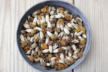 Dried marigold flowers in a round tin bowl placed on wooden table. Space for copy.