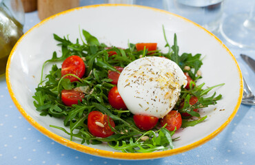 Close up of salad with burrata italian cheese, cherry tomatoes and arugula green leaf at plate