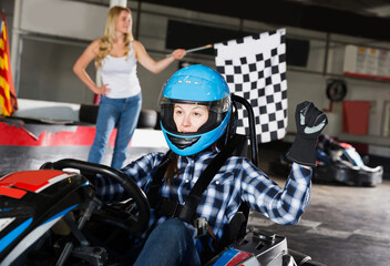 happy woman driving sport car for karting in sport club, woman with race flag on background