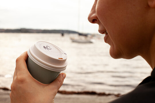 close up shot of a woman holding a cup of coffee with initials AC by the beach