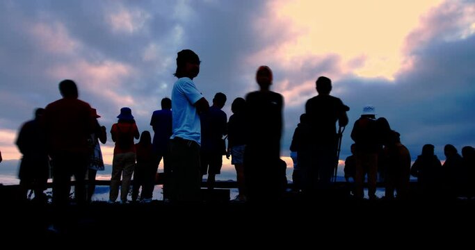 Silhouettes of tourist crowd waiting for the sunrise and doing activity, taking a photo, selfie with nature on the hill at viewpoint in time lapse shot.