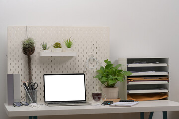 Computer laptop, supplies and houseplant on white desk in home office.