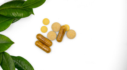 Herbal pills and capsule with leaves from fresh green source herbs in a display set against a white background.
