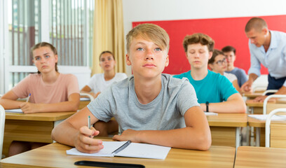 Fototapeta na wymiar Portrait of focused teenage student writing lectures in workbooks in classroom during lesson..