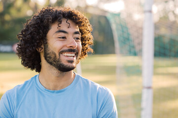 Close up photo of a smiling man with curly hair with beard wearing blue shirt on a sunny day