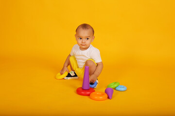 a little boy in a white T-shirt and yellow shorts plays with blocks pyramid toys