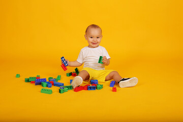 a little boy in a white T-shirt and yellow shorts plays with blocks pyramid toys