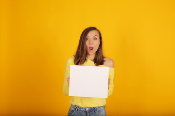 Fototapeta na wymiar a young beautiful blonde girl in a yellow jacket and jeans holds a white sheet of paper in her hands