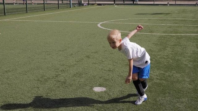 A little boy is playing soccer on the football field, he hits the ball on goal.