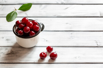 Ripe cherries in a white mug and next to it on a white wooden background. A place to copy. Close-up