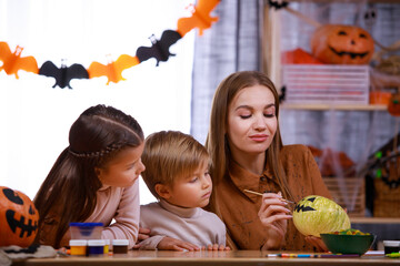 Mom draws a scary muzzle on a Halloween pumpkin for carving a lantern and shows it to the children. Happy family at home preparing for Halloween by making decorations. Family holiday. Close up.