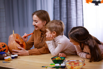 Naklejka premium Mom carves Jack lantern out of a pumpkin, and daughter and son are watching closely. The family is sitting at a table in the room. Halloween. Happy family party at home. Close up.