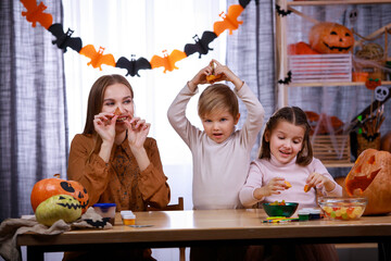 Happy family is preparing for Halloween at home. Mom, daughter and son are sitting at the table and playing with carved pumpkin cutters. Happy family party at home. Close up.