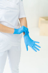 Medical concept. Nurse doctor surgeon dentist without face wear white costume puts on rubber disposable sterile blue gloves isolated on white soft blure background. Verical photo. Focus on hands,