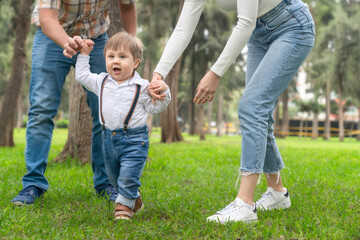 Fototapeta premium Parents helping a child to walk outdoors