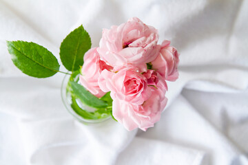 View from directly above of small bouquet of roses in a glass vase; Bouquet of pink roses on a crumpled cloth