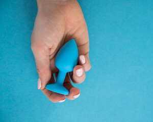 A woman is holding a blue anal plug on a blue background. Adult toy for alternative sex - obrazy, fototapety, plakaty