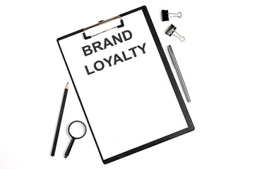 On a white background magnifier, a pen and a sheet of paper with the text BRAND LOYALTY .Business concept