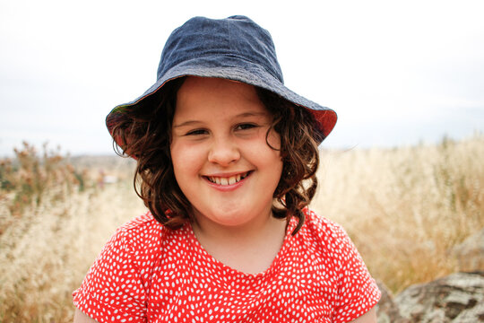 Mid-shot of young girl in grassy field wearing a red dress and blue bucket hat
