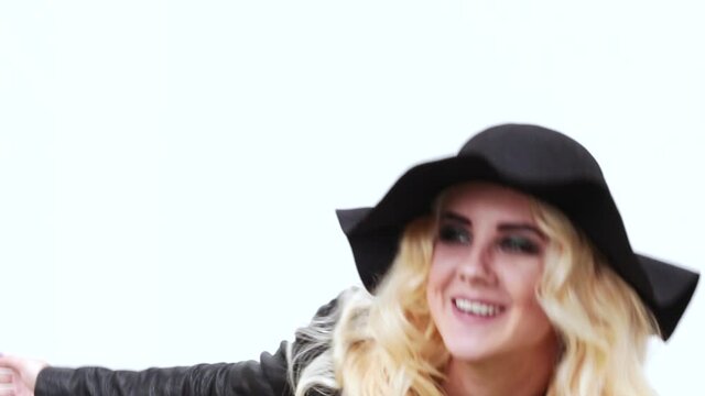 Beautiful blonde girl in a black hat and black leather jacket looks at the camera and sends an air kiss. Video