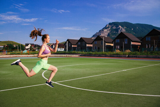 A young woman jumps on a football field. A girl at the stadium is engaged in sports.A healthy lifestyle.
