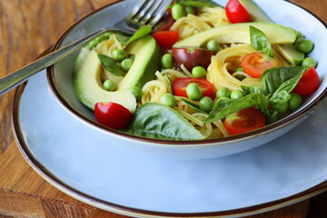 Pasta salad with green peas, avocado, cherry tomatoes and basil on rustic wooden background. Top view