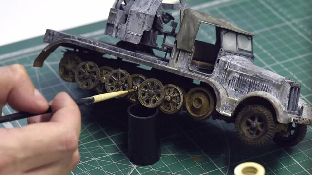 Scale Modeling. Close-up of a male's hand painting the wheel of a WWII military car. Hobby and leisure at home. A man making finishing paint touches in the coloring and decoration of the wheel.