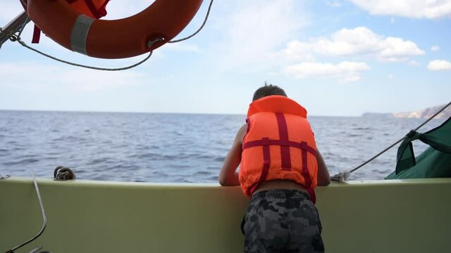 little kid in orange lifejacket on board during summer boat sailing in open sea